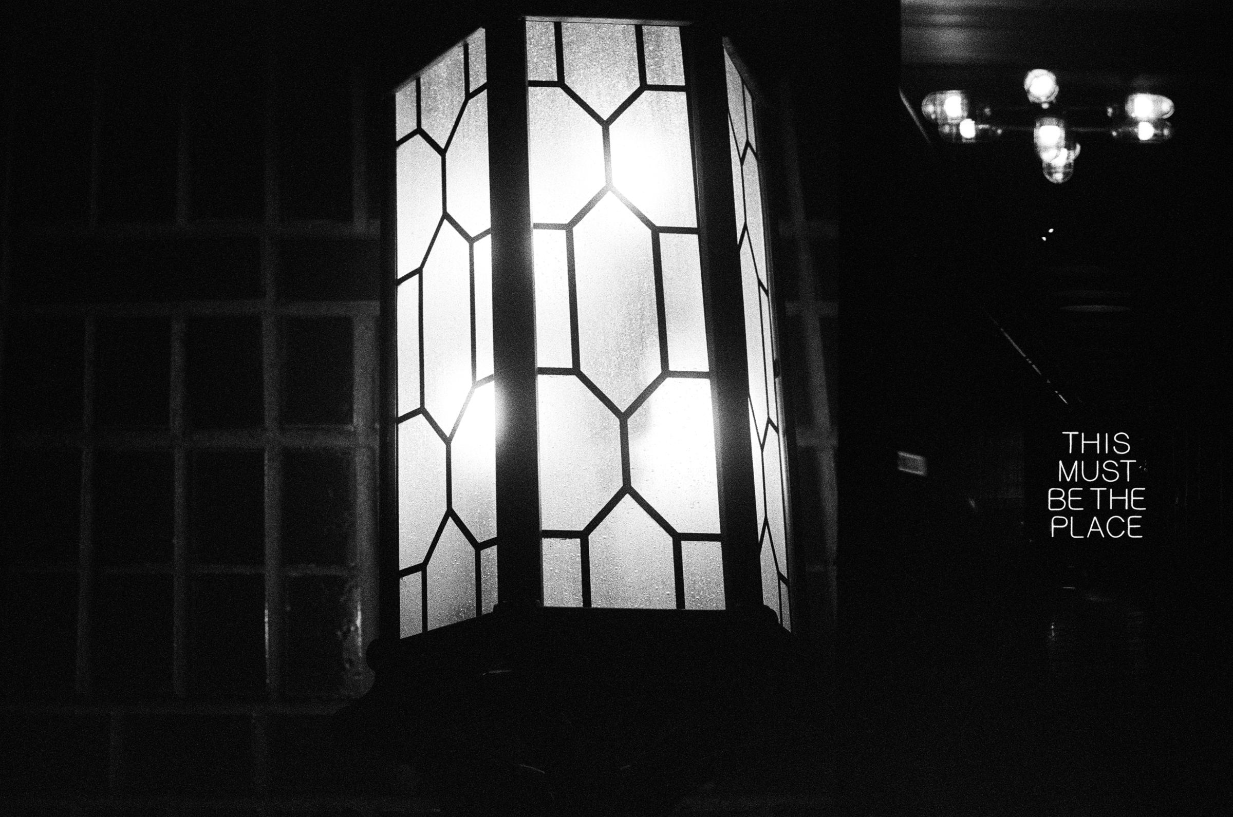 A leaded-glass lantern glowing in a dark room; a neon sign reads This Must Be The Place