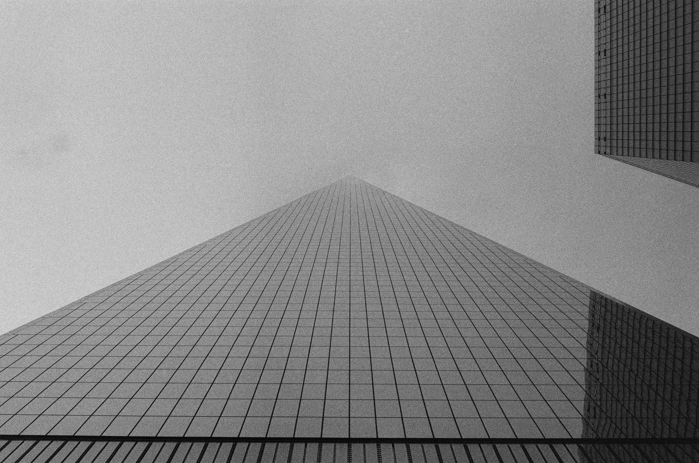 Looking straight up a glass tower into flat grey sky